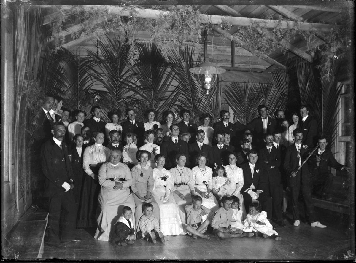 A community group gathered on a decorated hall stage in Piha, early 1900s